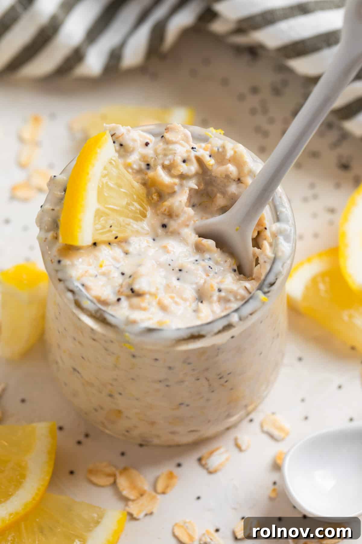 Sunshine Lemon Poppy Seed Overnight Oats 6 A white ceramic spoon scooping into a glass jar of lemon poppy seed overnight oats, showing the creamy texture.