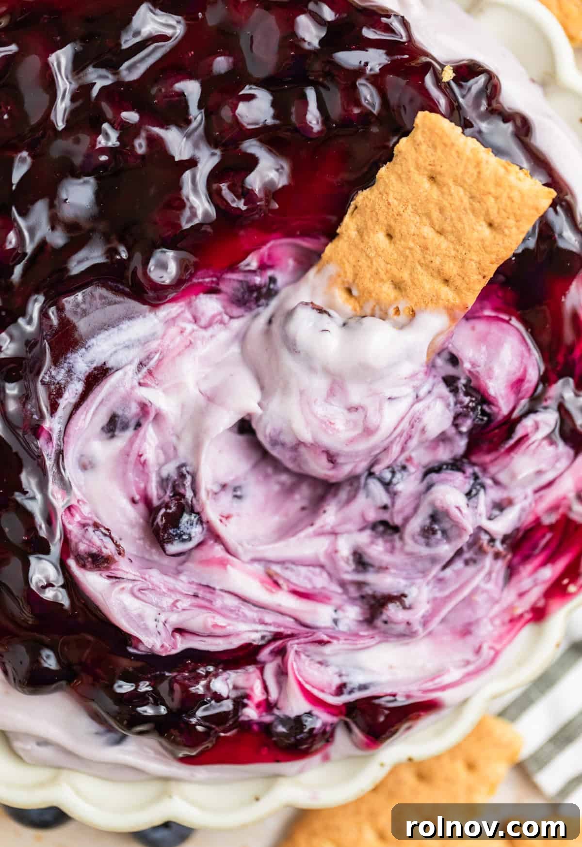 Dreamy Blueberry Cheesecake Dip 2 Graham cracker enthusiastically dipped into a bowl of creamy blueberry cheesecake dip, garnished with fresh blueberries.