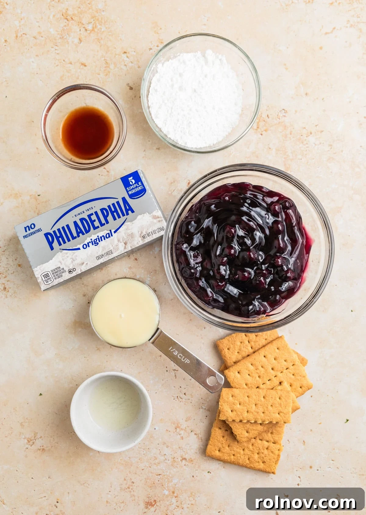 Dreamy Blueberry Cheesecake Dip 3 Arrangement of key ingredients for blueberry cheesecake dip: softened cream cheese, blueberry pie filling, powdered sugar, sweetened condensed milk, vanilla extract, and a fresh lemon.