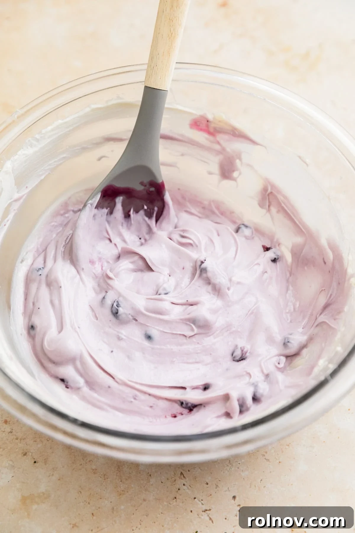 Dreamy Blueberry Cheesecake Dip 7 Finished blueberry cheesecake dip presented in a clear glass bowl with a serving spoon, generously topped with remaining blueberry filling.