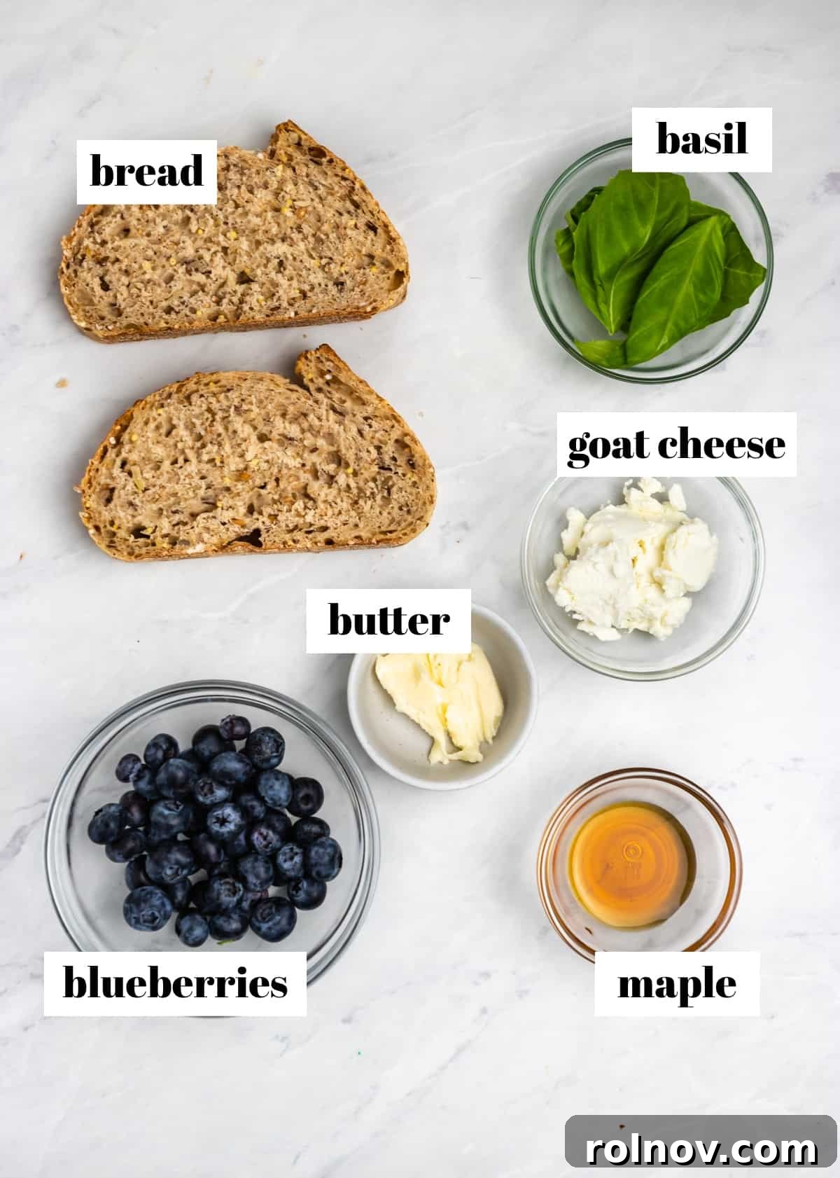 Sweet & Savory Blueberry Basil Goat Cheese Grill 3 Ingredients for Blueberry Basil Goat Cheese Grilled Cheese laid out on a kitchen counter: bread, a bowl of blueberries, a small bowl of honey, a bunch of fresh basil, a log of goat cheese, and a stick of butter.