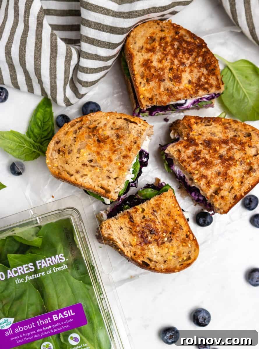 Sweet & Savory Blueberry Basil Goat Cheese Grill 7 Overhead view of two halves of a Blueberry Basil Goat Cheese Grilled Cheese Sandwich, served on a plate with a striped napkin, showcasing the vibrant filling.