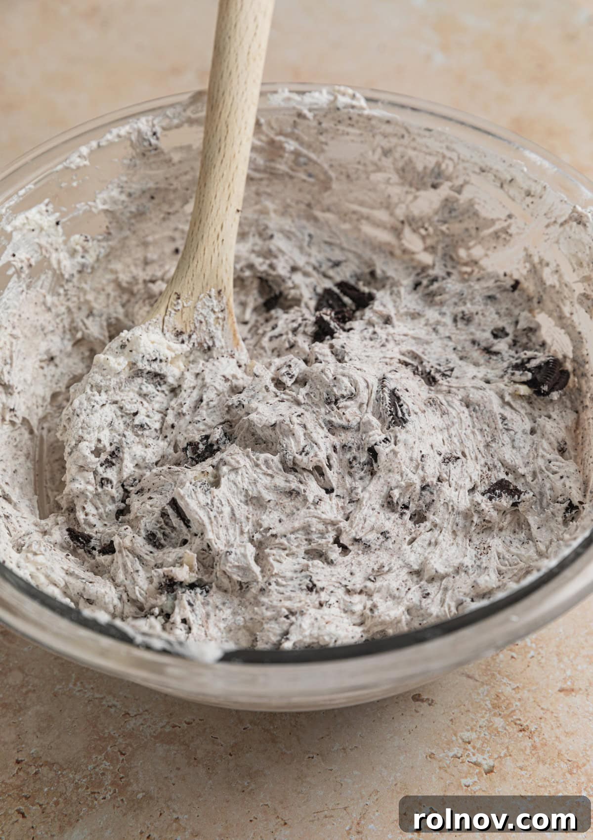 Effortless Oreo Cheesecake Treats 11 A bowl filled with the completed no-bake Oreo cheesecake filling, studded with cookie pieces, with a spoon ready for scooping.