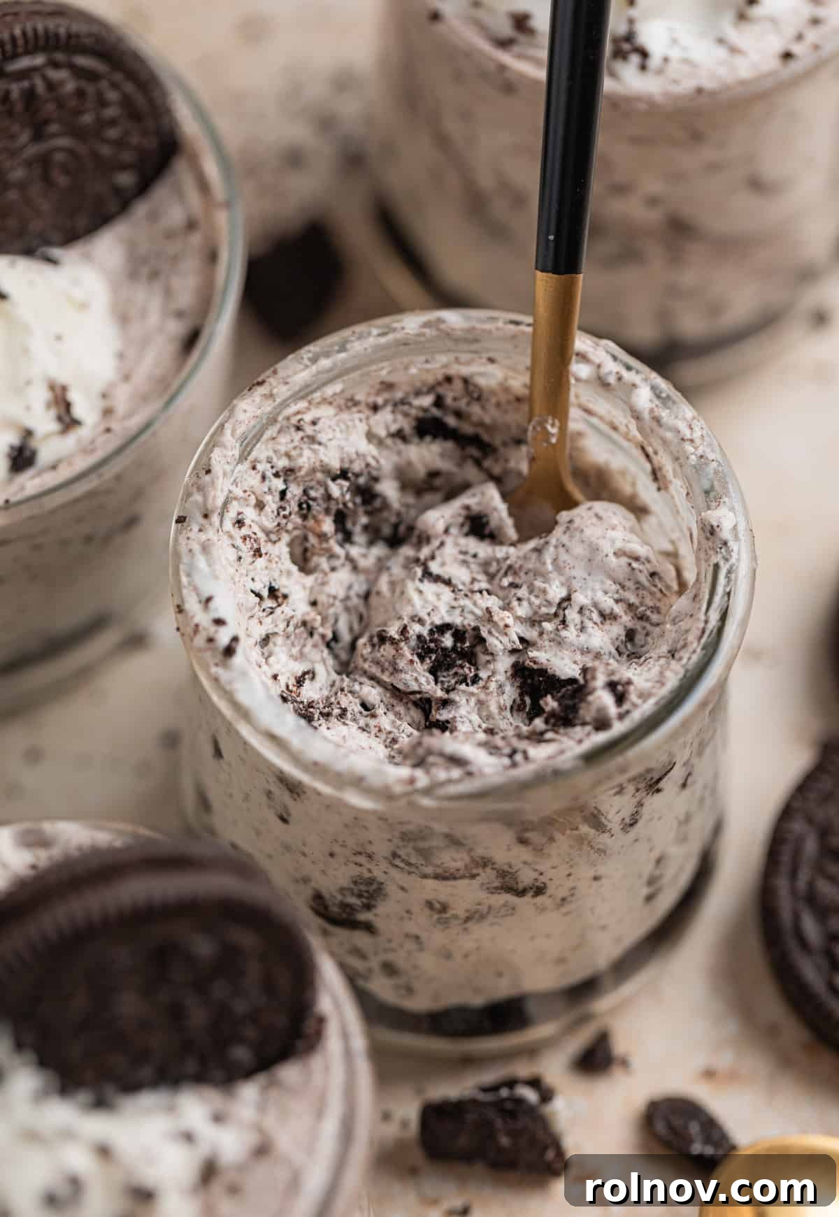 Effortless Oreo Cheesecake Treats 13 A close-up shot of a spoon dipping into a glass dessert cup filled with the creamy no-bake Oreo cheesecake mixture, garnished with crumbs.