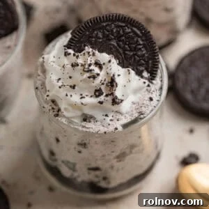 Oreo cheesecake cups topped with whipped cream and an Oreo along with more cookie crumbs.