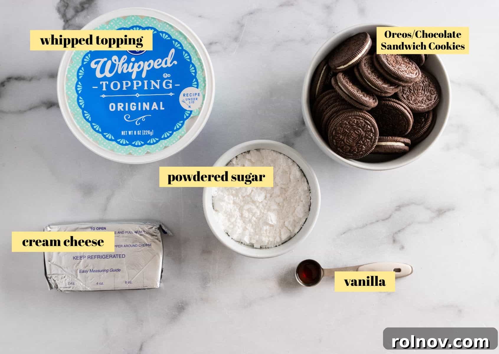 Effortless Oreo Cheesecake Treats 3 A simple flat lay photo showing the five main ingredients for no-bake cheesecake cups: a block of cream cheese, a tub of Cool Whip, a bag of powdered sugar, a bottle of vanilla extract, and a package of Oreo cookies.