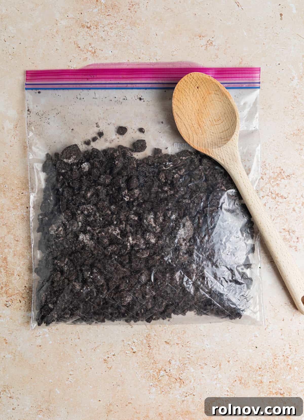 Effortless Oreo Cheesecake Treats 5 Crushed Oreo cookies inside a plastic bag, with a wooden spoon resting on top, showing the desired crumb texture.
