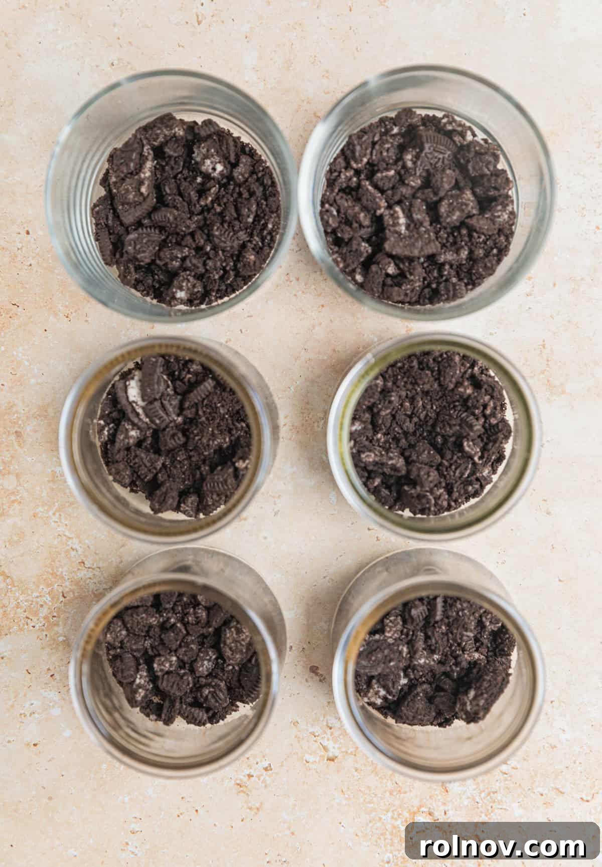Effortless Oreo Cheesecake Treats 6 Six individual glass dessert jars, each with a layer of crushed Oreo cookies at the bottom, prepared for the cheesecake filling.