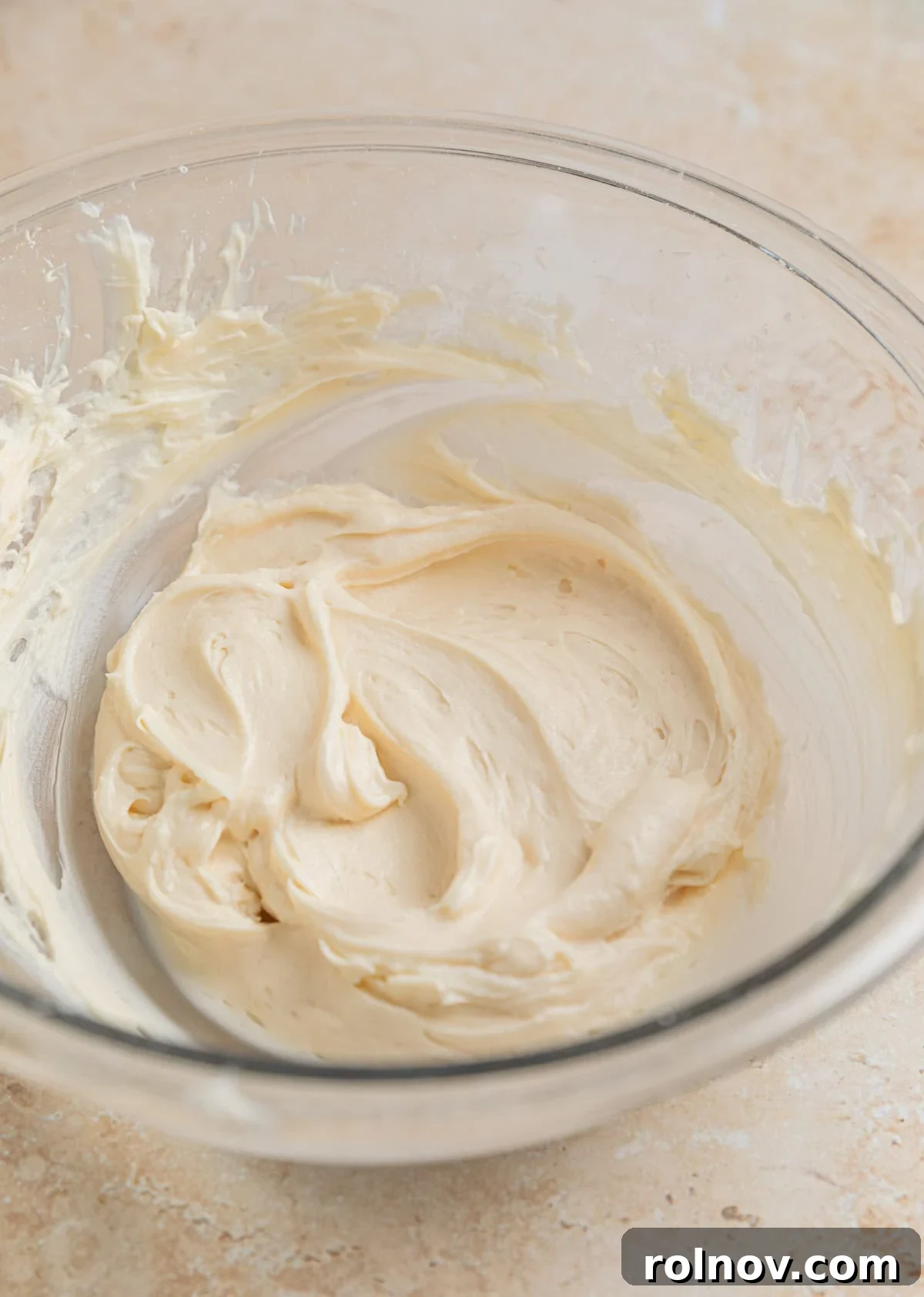Effortless Oreo Cheesecake Treats 7 Softened cream cheese and powdered sugar being creamed together in a glass mixing bowl with an electric mixer.