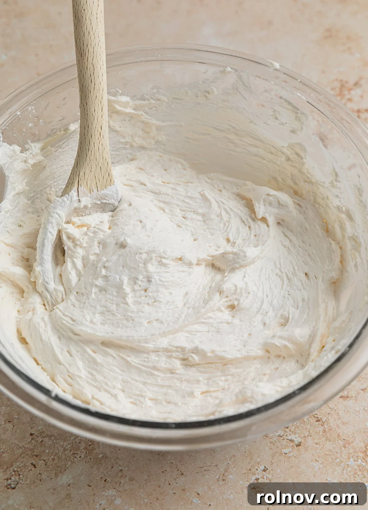 Effortless Oreo Cheesecake Treats 9 The finished smooth and creamy no-bake cheesecake mixture in a glass bowl, with a wooden spoon resting in it.