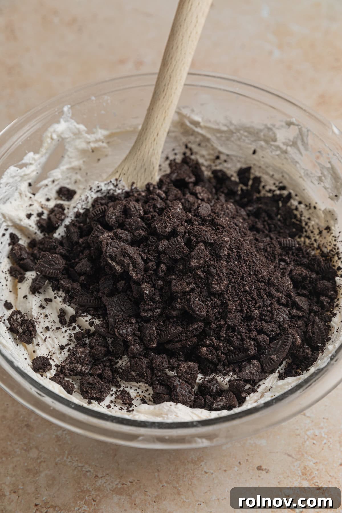 Effortless Oreo Cheesecake Treats 10 Additional crushed Oreos being folded into the creamy no-bake Oreo cheesecake mixture in a mixing bowl.