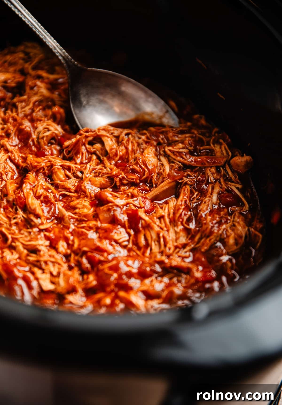 Effortless Slow Cooker BBQ Pulled Chicken 3 A slow cooker filled with perfectly shredded BBQ chicken, with a serving spoon poised to scoop out a delicious portion.