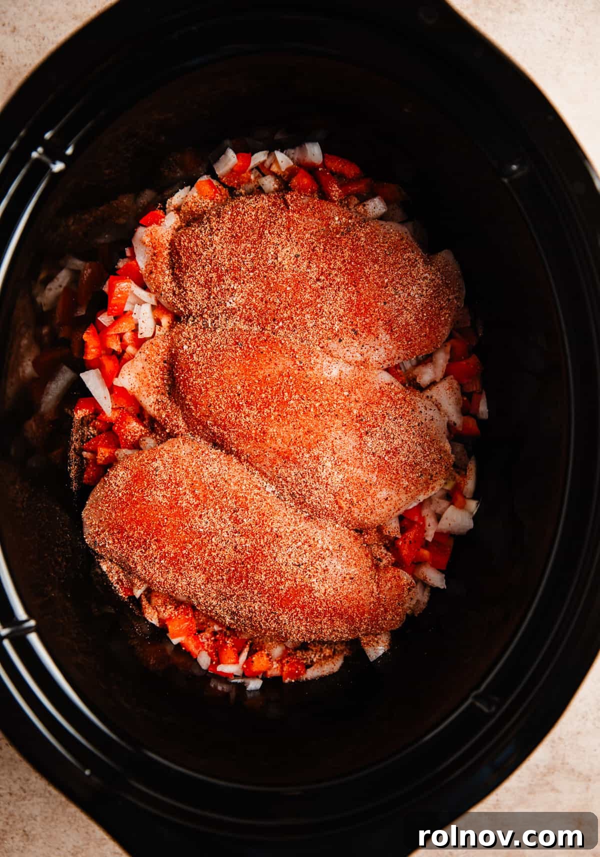 Effortless Slow Cooker BBQ Pulled Chicken 4 Chicken breasts seasoned with a spice rub, placed over chopped onions and peppers in a slow cooker.