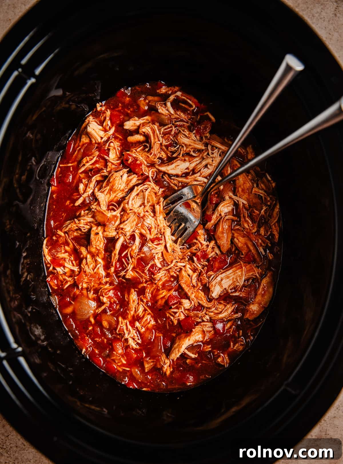 Effortless Slow Cooker BBQ Pulled Chicken 7 Shredded BBQ chicken in a slow cooker pot, with two forks demonstrating its tender texture.