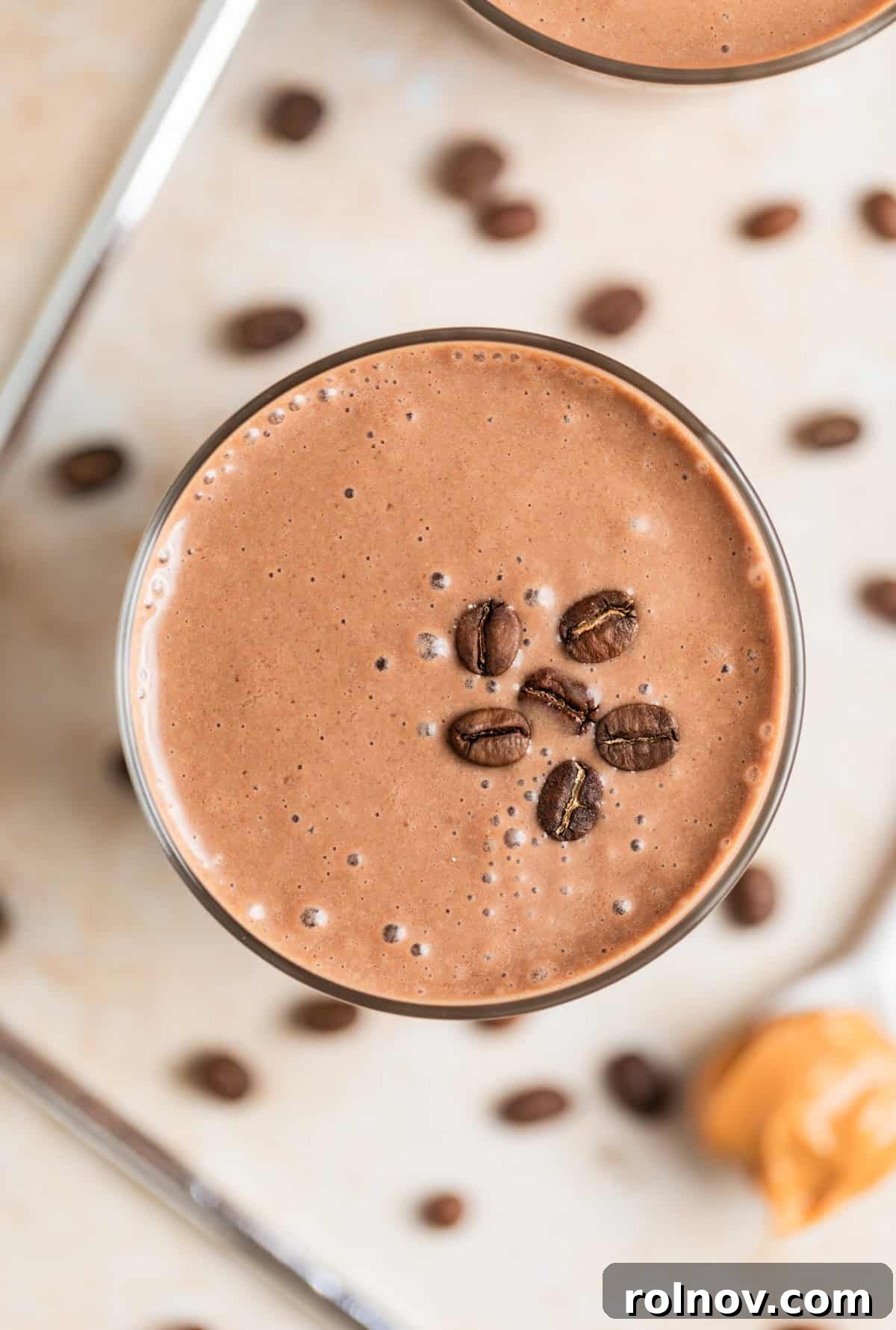 Peanut Butter coffee smoothie with peanut butter on spoon and coffee beans beside the glass. 