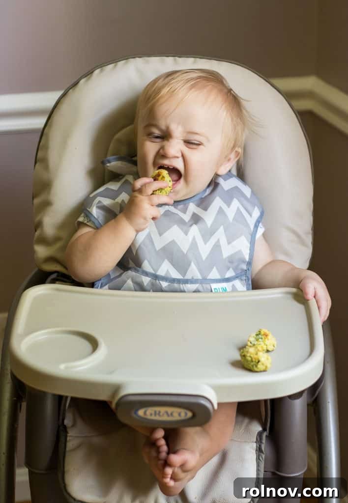 Zucchini Cheese Poppers 4 Close-up of a baby's hands exploring a Cheesy Zucchini Tot, highlighting sensory food experiences for children.