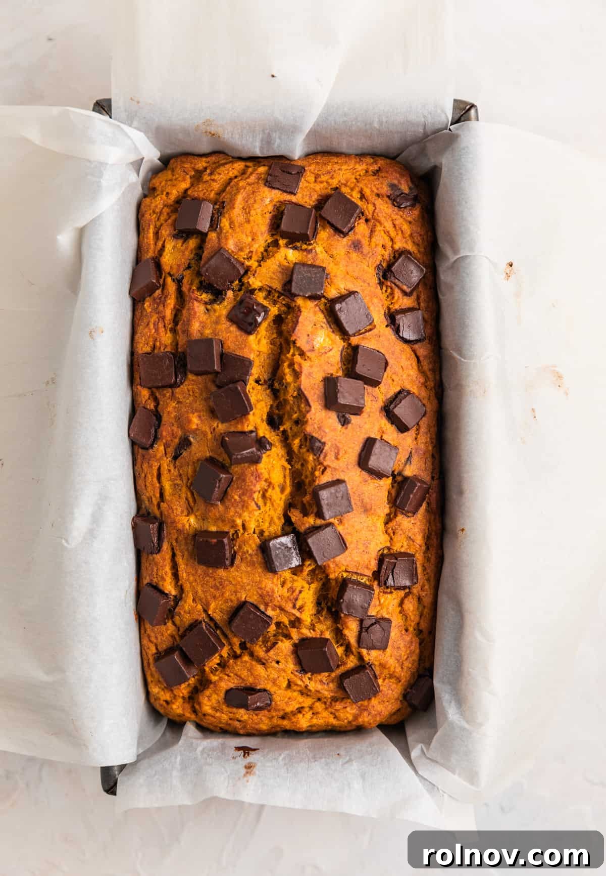 Pumpkin Speckled Banana Bread 7 Baked pumpkin chocolate chip banana bread in bread pan lined with parchment paper.