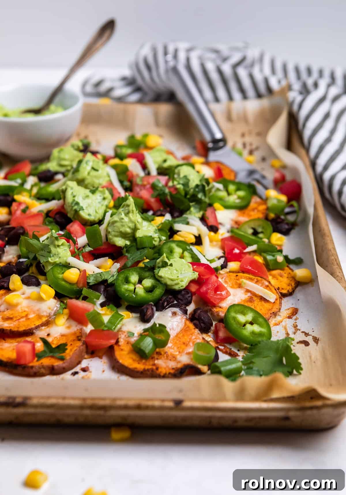 Sheet pan with sweet potato nachos topped with beans, corn, cilantro and avocado crema, ready to serve.