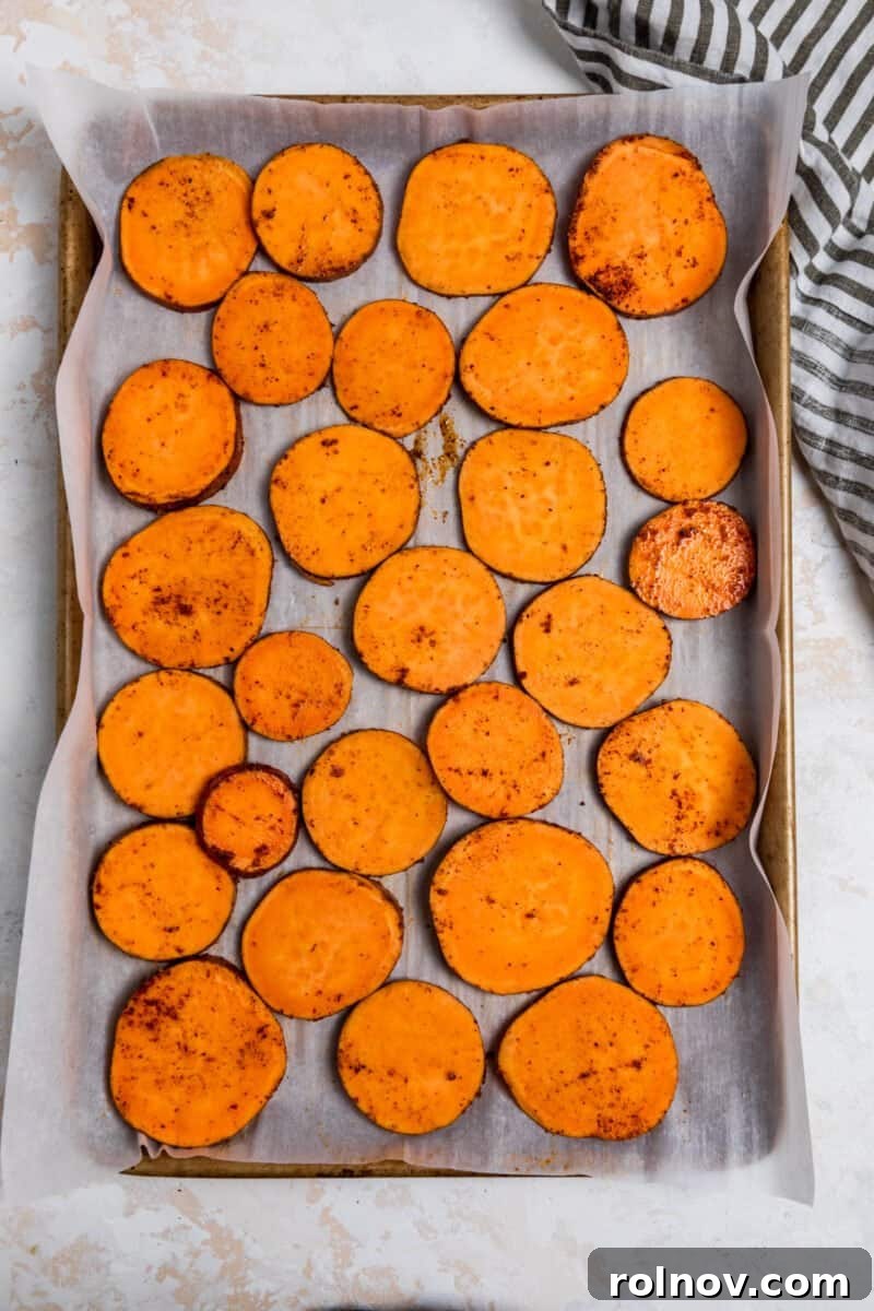 Seasoned sweet potato slices perfectly arranged on a parchment-lined baking sheet.
