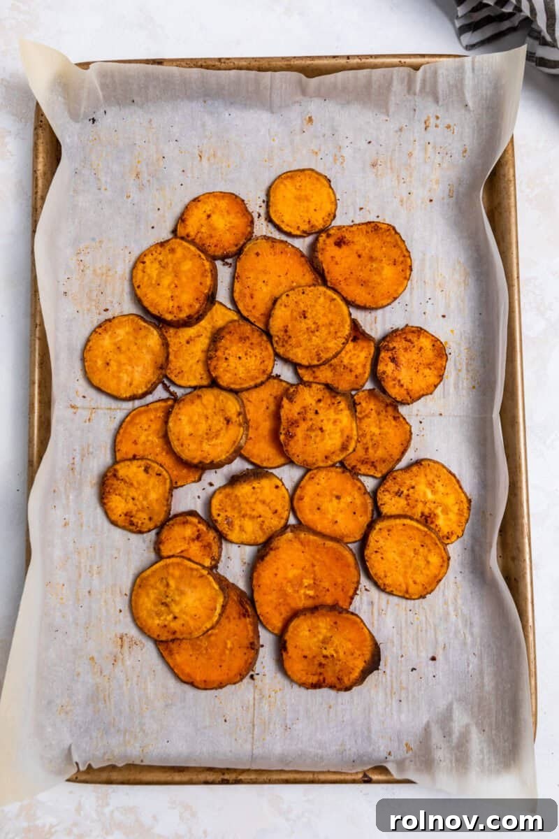 Roasted sweet potato rounds pulled together in the center of a parchment-lined baking sheet, ready for toppings.