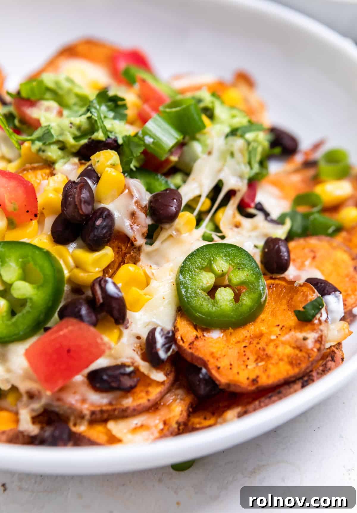 White bowl brimming with sweet potatoes, corn, cheese, beans, and various other fresh ingredients, ready to be enjoyed.