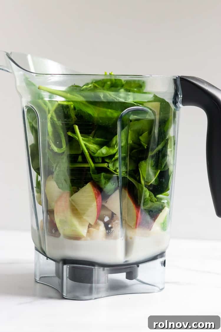 Green Dream Apple Pie Smoothie 4 Fresh ingredients for a healthy apple pie smoothie, including spinach, apple, and a frozen banana, arranged in a blender, ready to be processed.