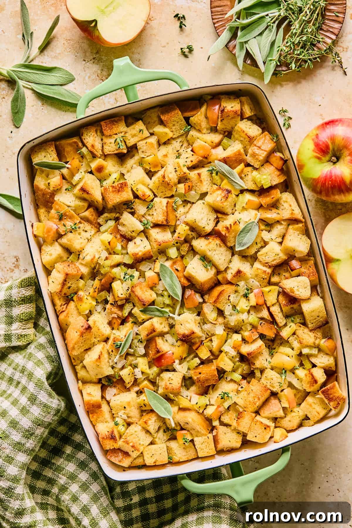 Homestyle Apple Sage Stuffing 2 Golden-brown Apple Sage Stuffing in a baking pan, garnished with fresh chopped herbs and sage leaves.