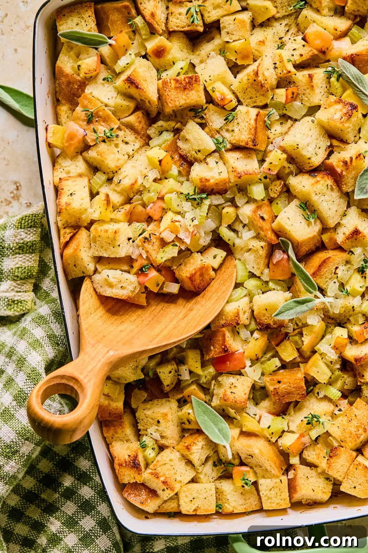 Homestyle Apple Sage Stuffing 13 A serving spoon scooping into a pan of golden apple sage stuffing, garnished with fresh parsley.