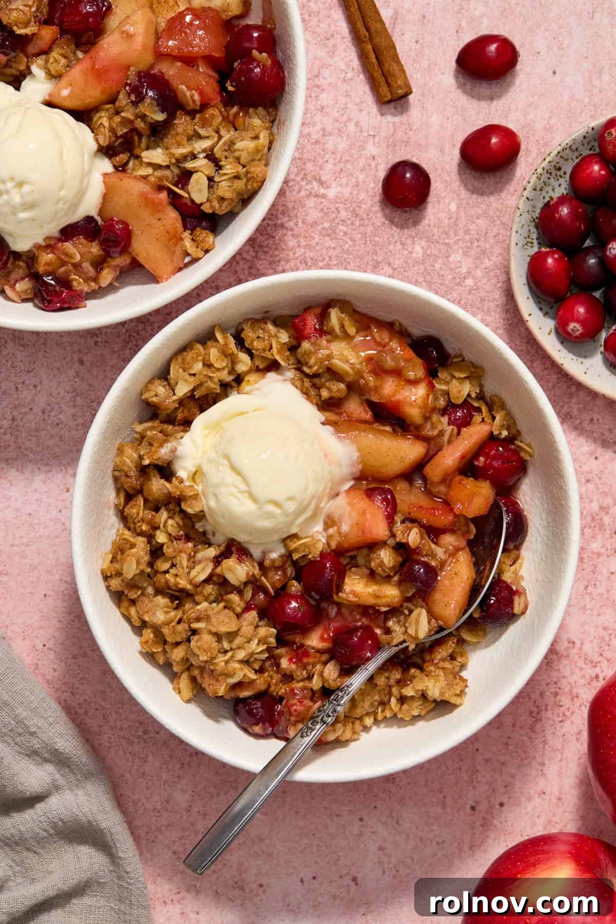 White bowls with serving of apple cranberry crisp topped with scoop of vanilla ice cream.