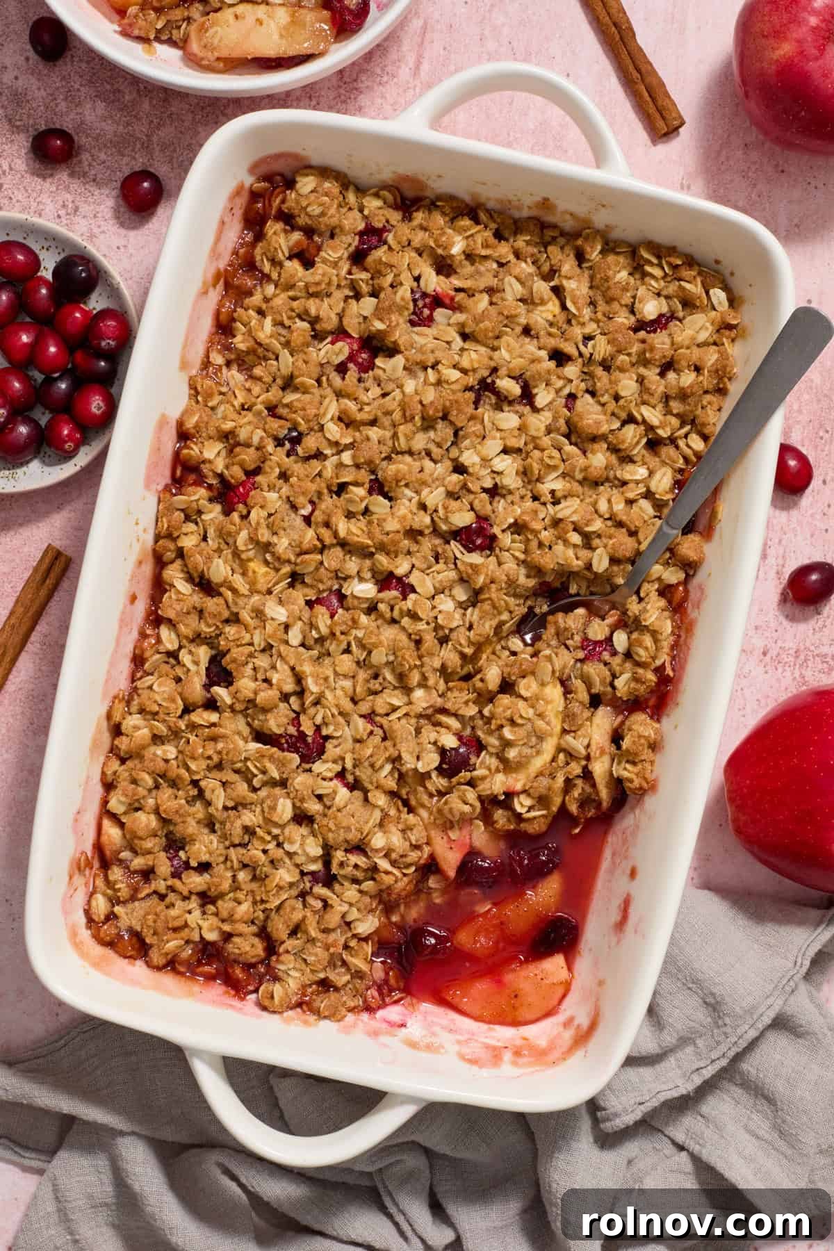 White baking pan with cranberry apple crisp with serving spoon scooping into the dessert.