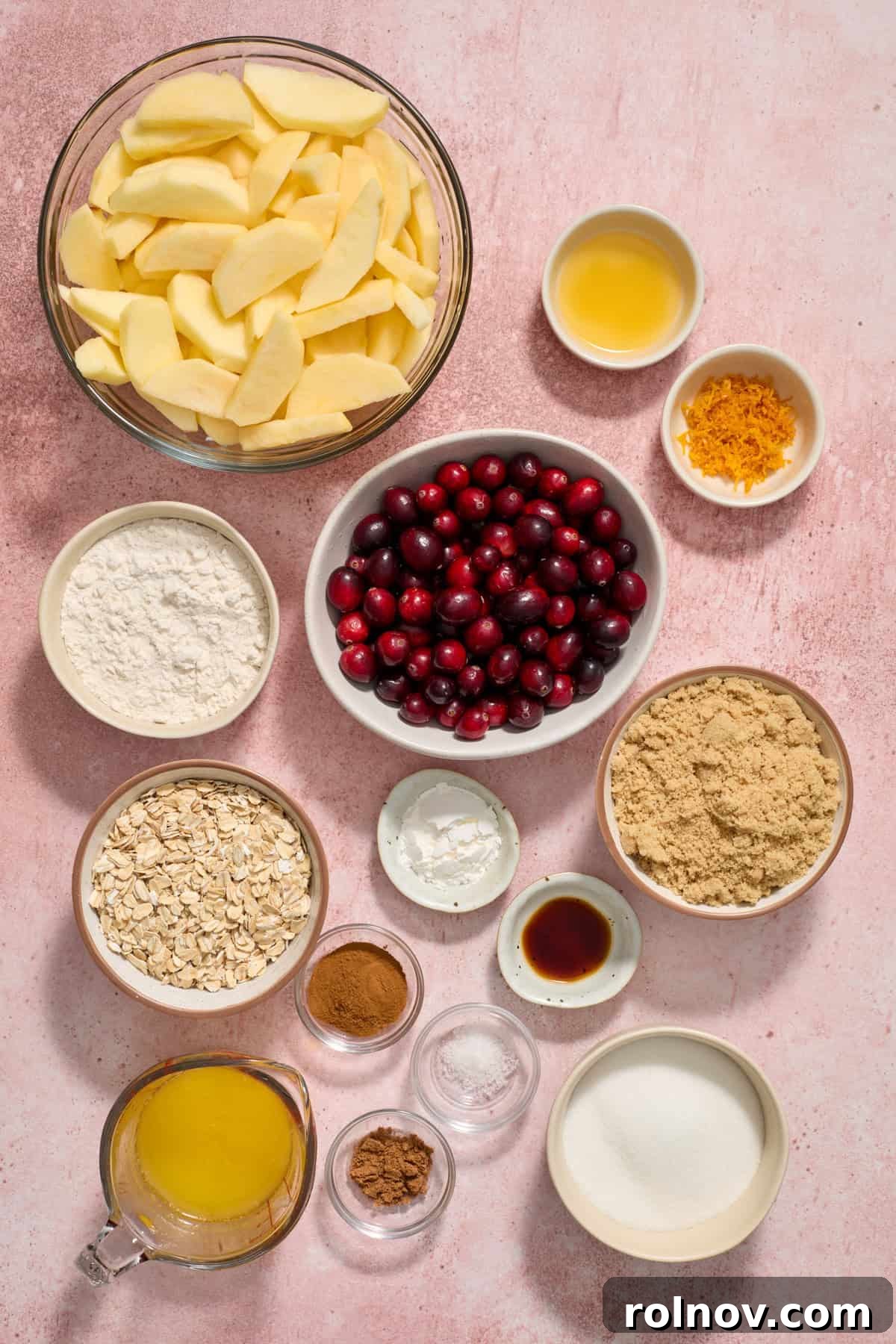 Sliced apples, orange zest, flour, butter, sugar and more arranged on surface.
