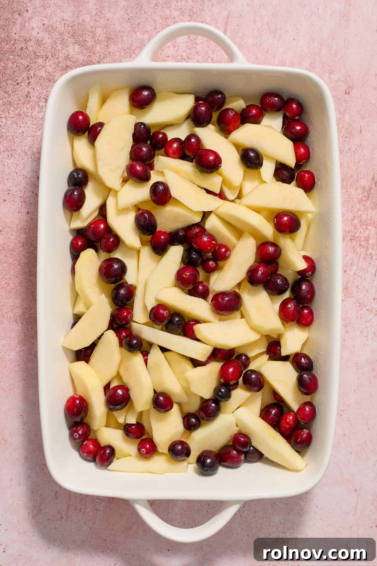 Cranberries and apples in white baking dish.