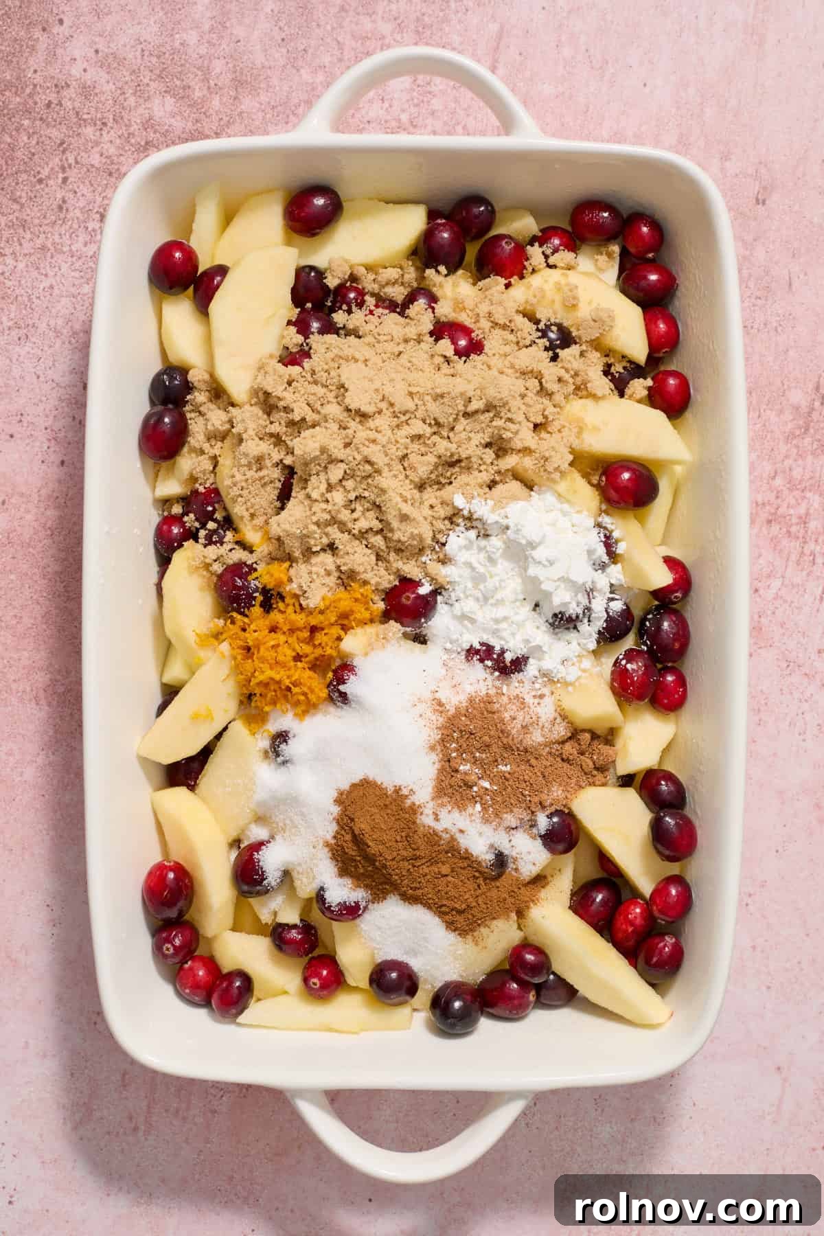 Cranberries, apples, cinnamon, orange zest, sugar and other ingredients in baking dish.
