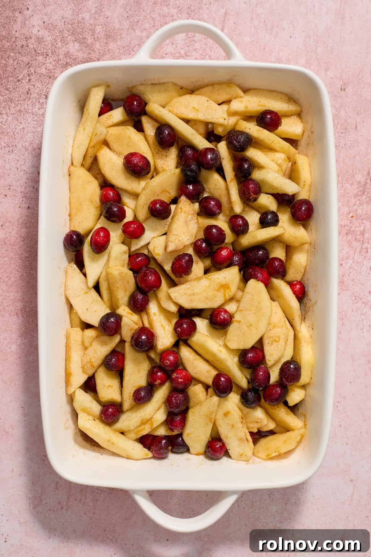Baking dish with cranberries, apples, sugar and spices tossed together.