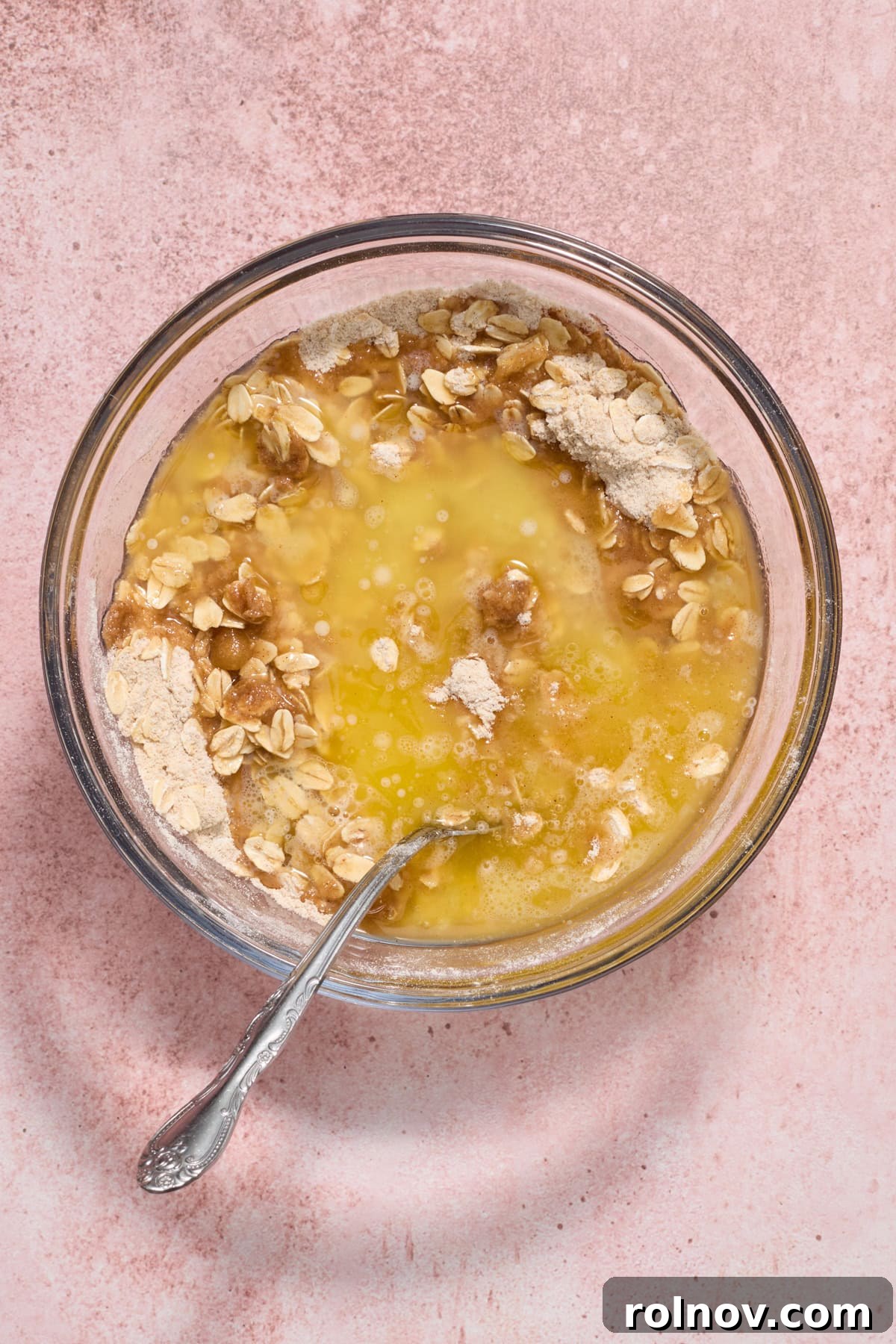 Butter, oats and flour in glass mixing bowl with spoon.