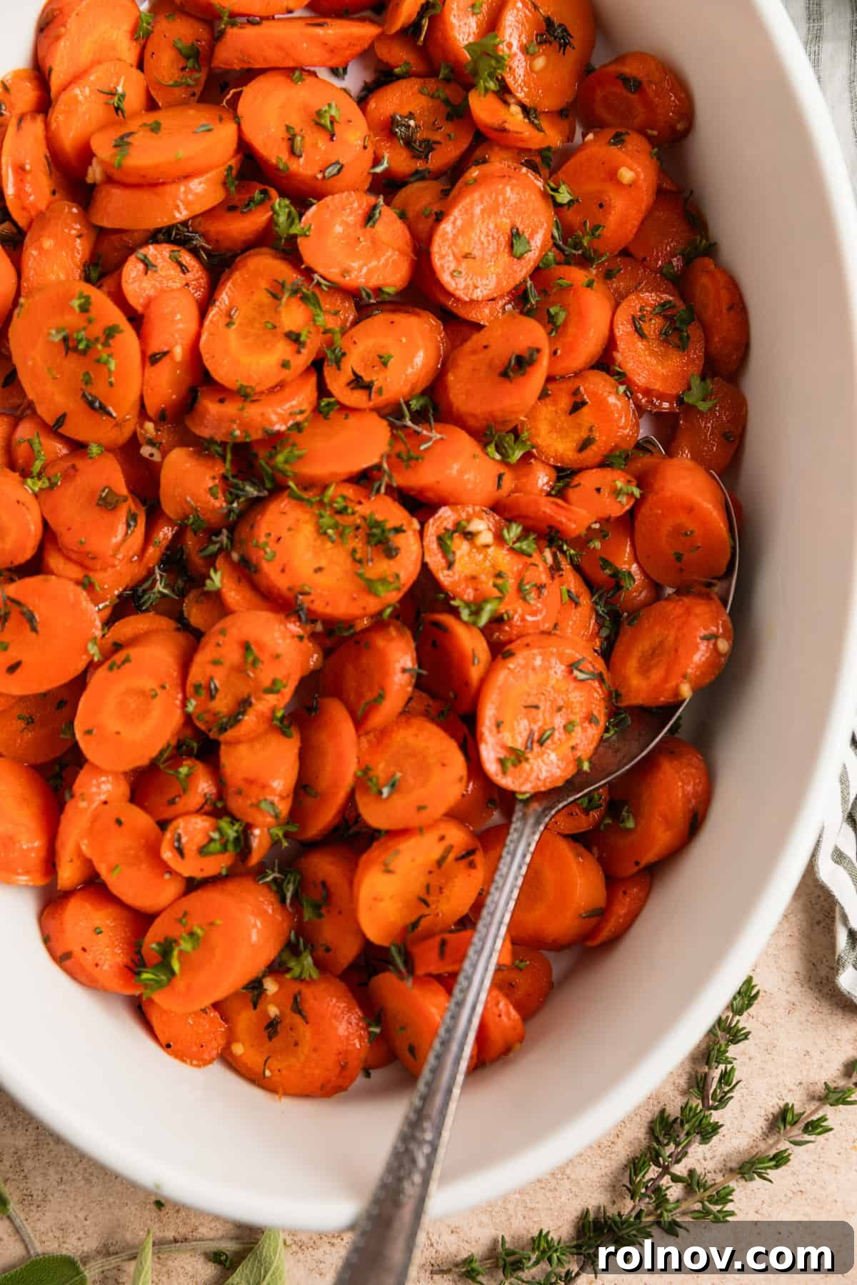 Sweet & Savory Maple Herb Roasted Carrots 2 Maple glazed herbed carrots with fresh herbs in white dish with serving spoon.