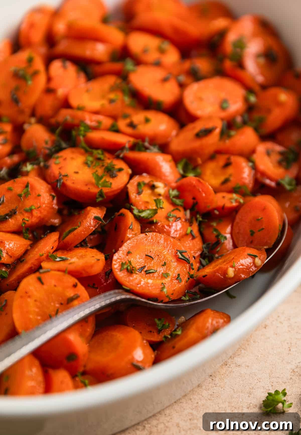 Sweet & Savory Maple Herb Roasted Carrots 3 Roasted carrots in white bowl with serving spoon.