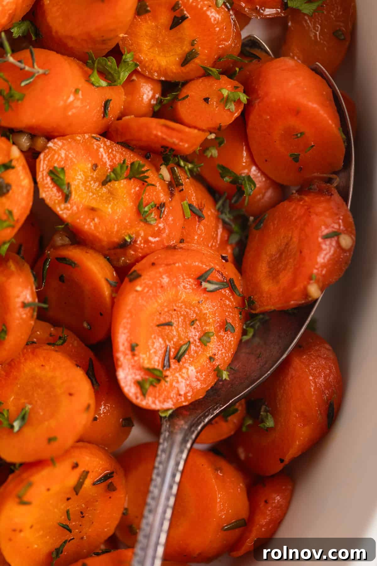 Sweet & Savory Maple Herb Roasted Carrots 4 Maple glazed herb roasted carrots in white serving dish topped with fresh parsley and thyme.