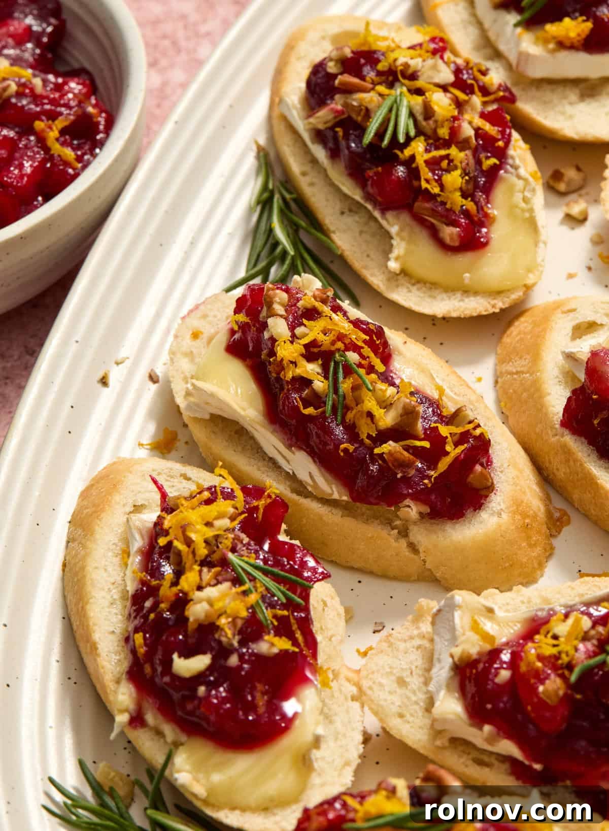 Cranberry Brie Crostini, garnished with fresh rosemary and orange zest, arranged beautifully on a serving platter.