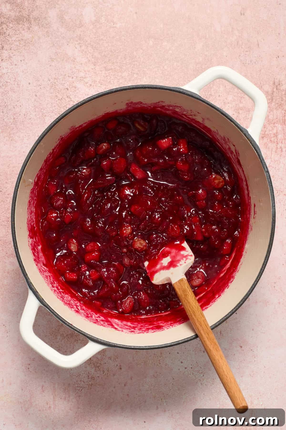 Simmering cranberry chutney in a pot, stirred gently with a wooden spatula, showing its thickening consistency.