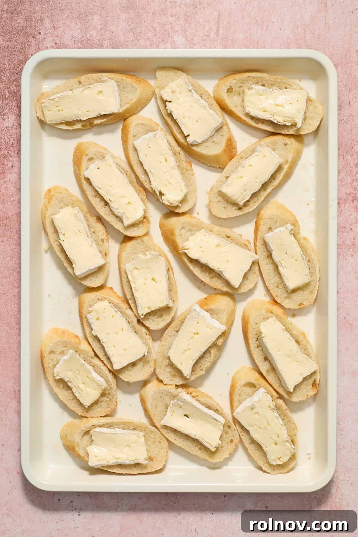 Slices of baguette arranged on a baking sheet, each topped with a delicate slice of brie cheese.