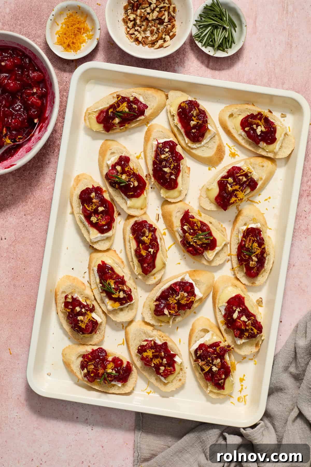 A baking sheet filled with an array of Cranberry Brie Crostini, fully prepped and garnished, ready for serving.