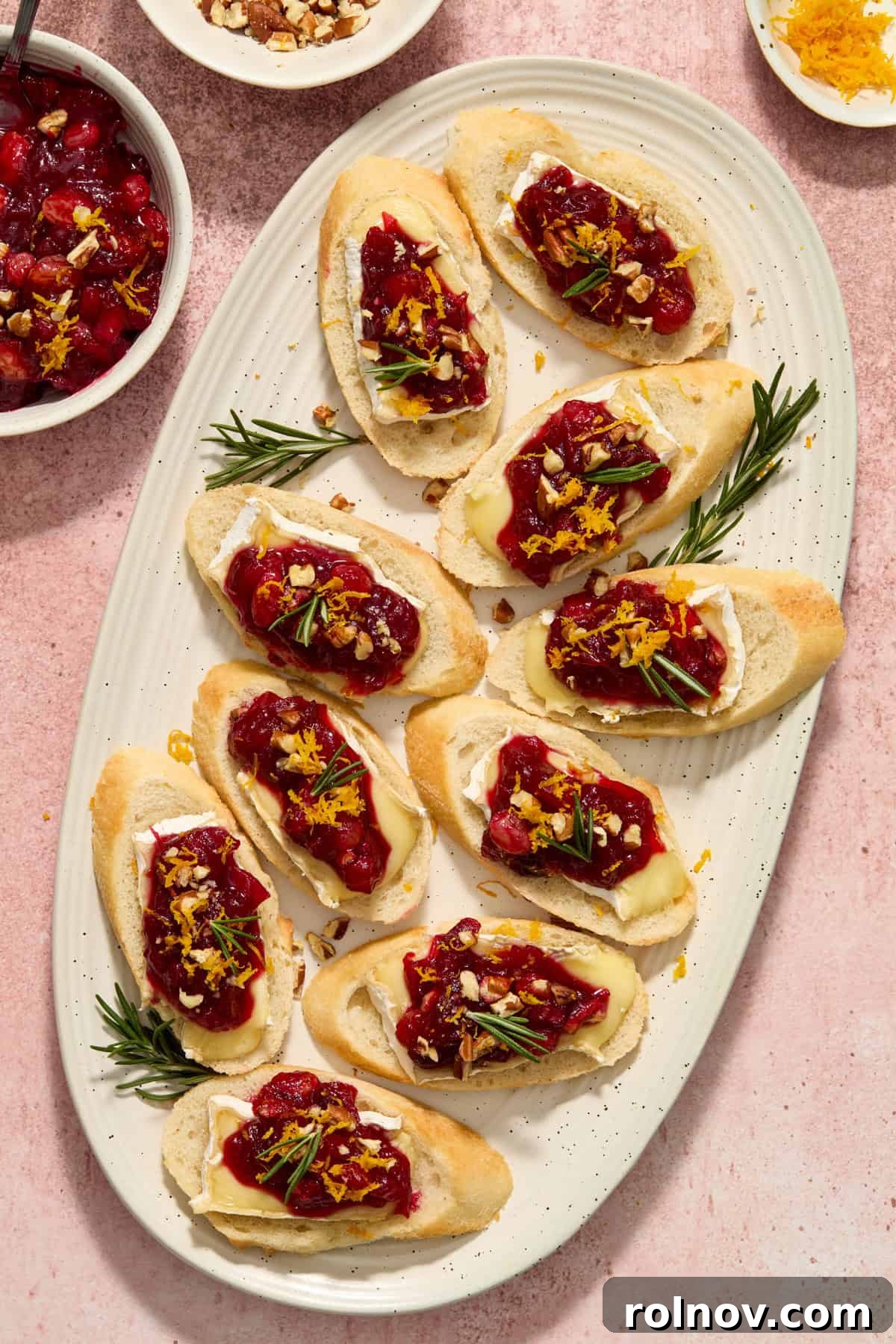 A elegant serving platter showcasing numerous Cranberry Brie Crostini, each perfectly topped with chutney, fresh herbs, and orange zest.