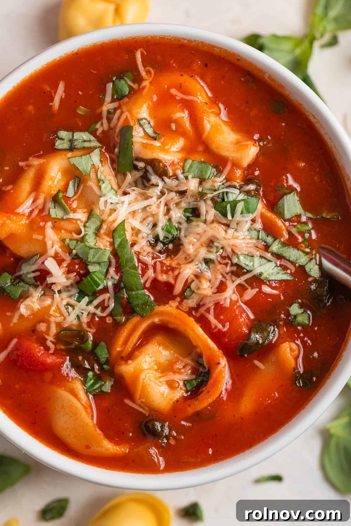Velvety Tomato Tortellini Soup 2 White bowl of tomato tortellini soup topped with fresh parmesan and chopped basil.