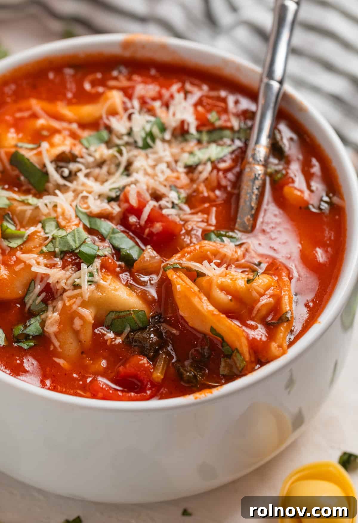 Velvety Tomato Tortellini Soup 7 Spoon scooping in soup with tortellini topped with parmesan and basil in spoon.