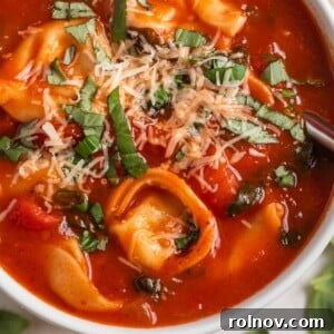 Velvety Tomato Tortellini Soup 8 White bowl with tomato tortellini soup and spoon scooping in.