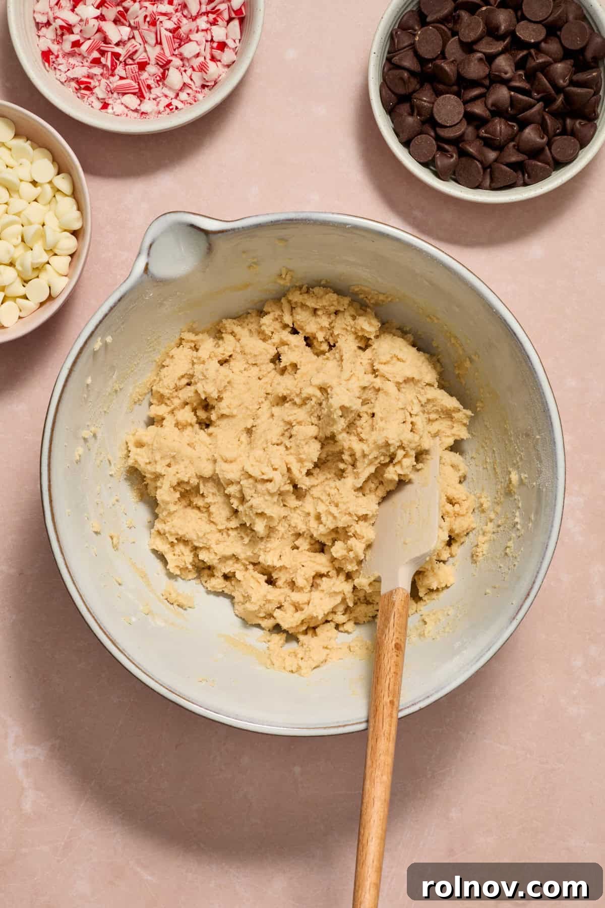 Cool Peppermint Chocolate Chip Cookies 10 Cookie dough in a bowl with a spatula, next to separate bowls of chocolate chips and crushed candy canes, ready to be folded in.