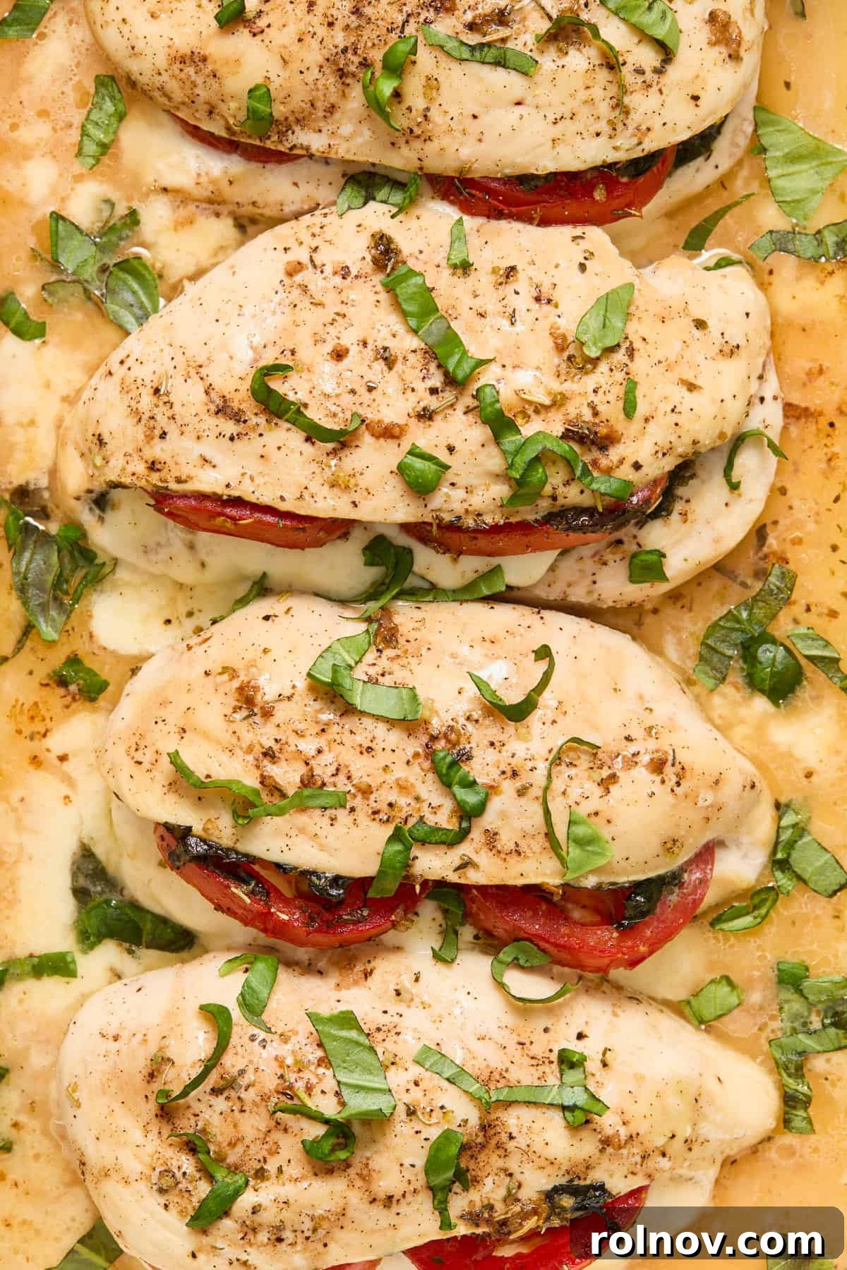 Chicken breast baking in a pan with melted mozzarella, tomato, and basil peeking out.
