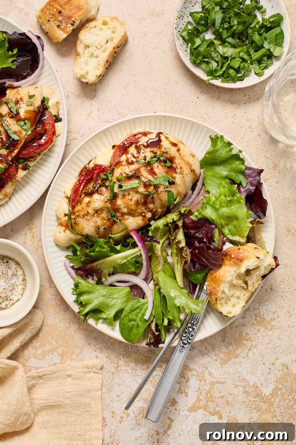 A plate featuring a cooked mozzarella stuffed chicken breast, accompanied by a fresh side salad and a piece of crusty bread. A fork and knife rest beside the plate.