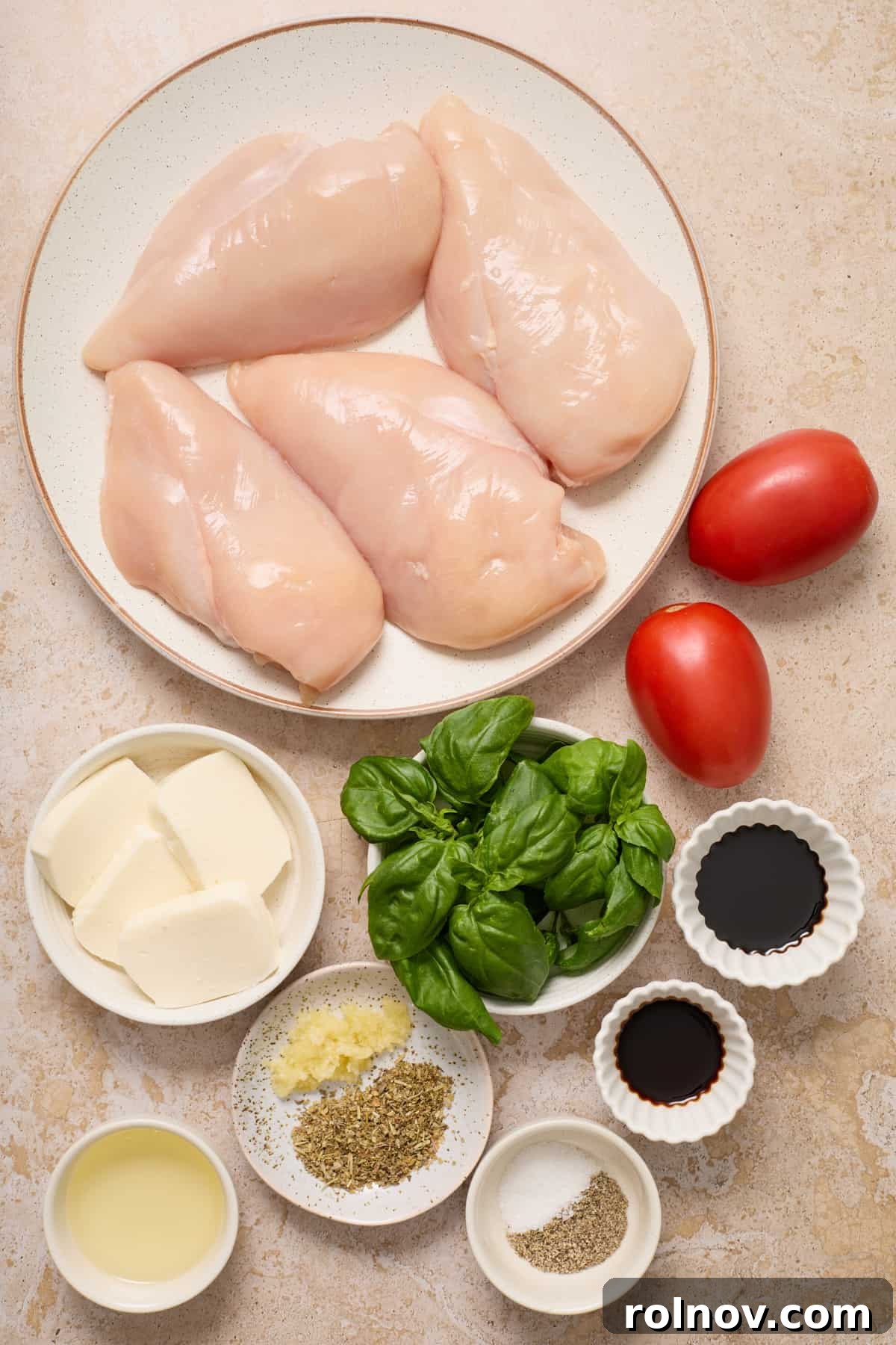 Chicken breast, fresh mozzarella slices, sliced Roma tomatoes, and basil leaves arranged with other ingredients for the recipe.